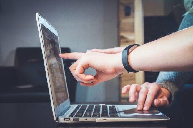 Open laptop with hands pointing to the screen.