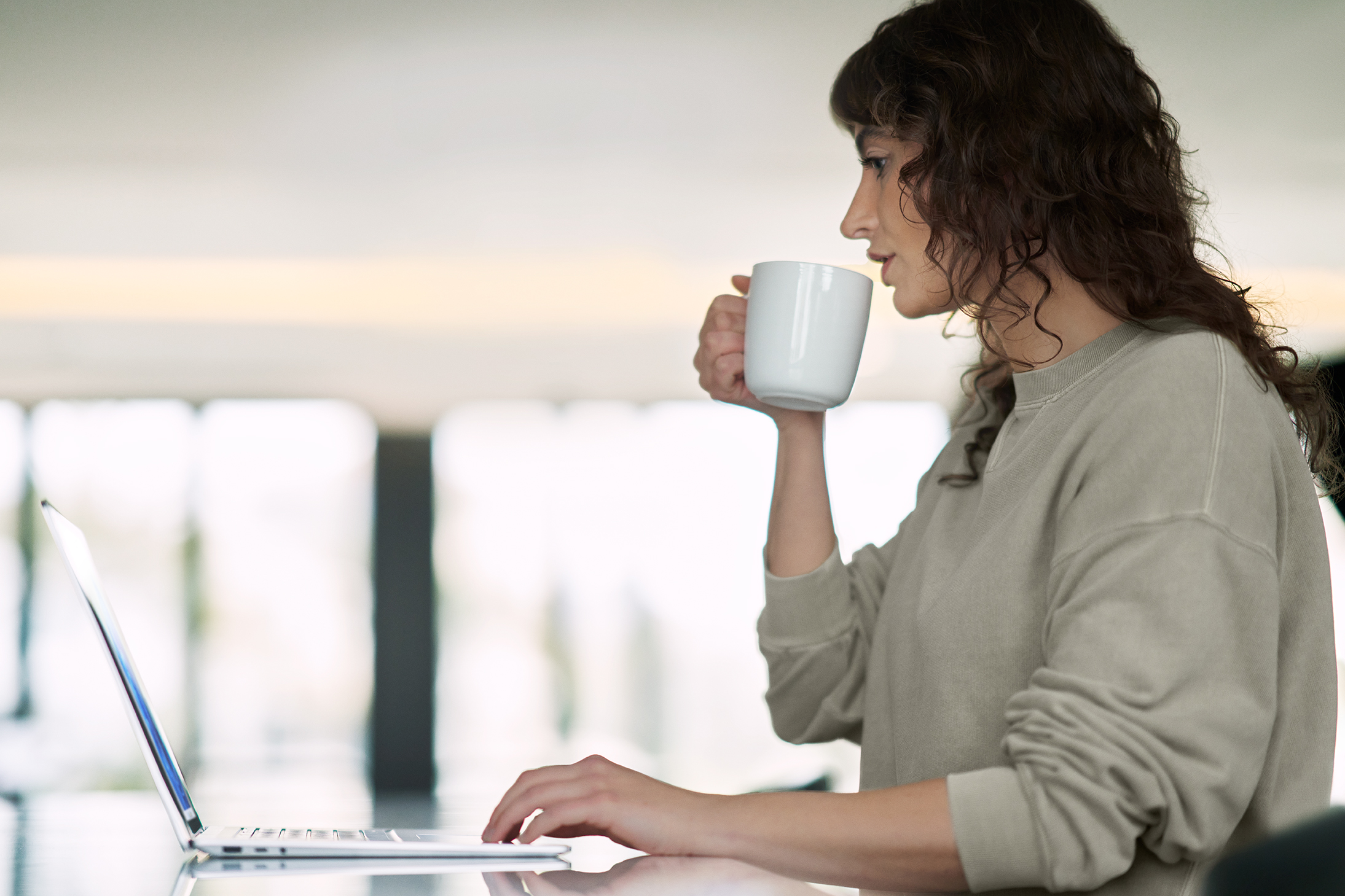 A teacher working on a laptop and drinking from a mug.