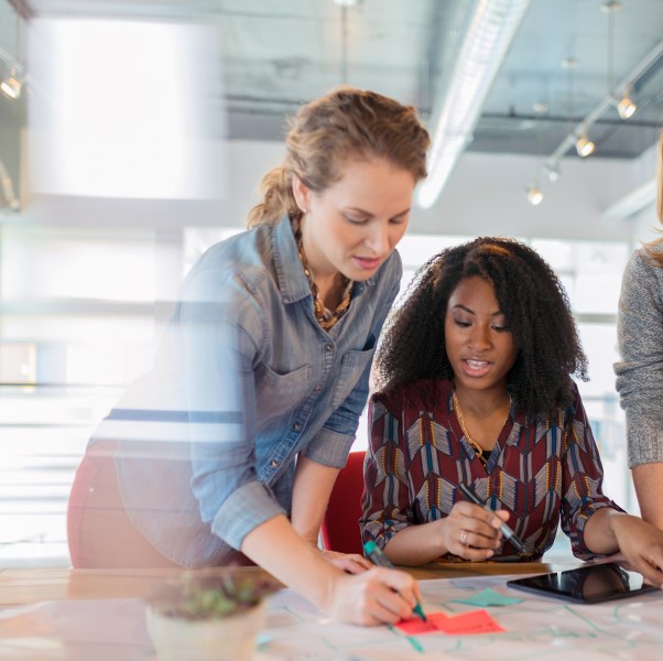 Businesswomen look at a digital tablet and discuss a project in their modern office.