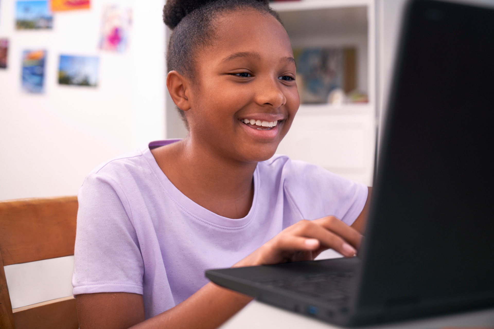 A student sitting at a table at home and working on a laptop.