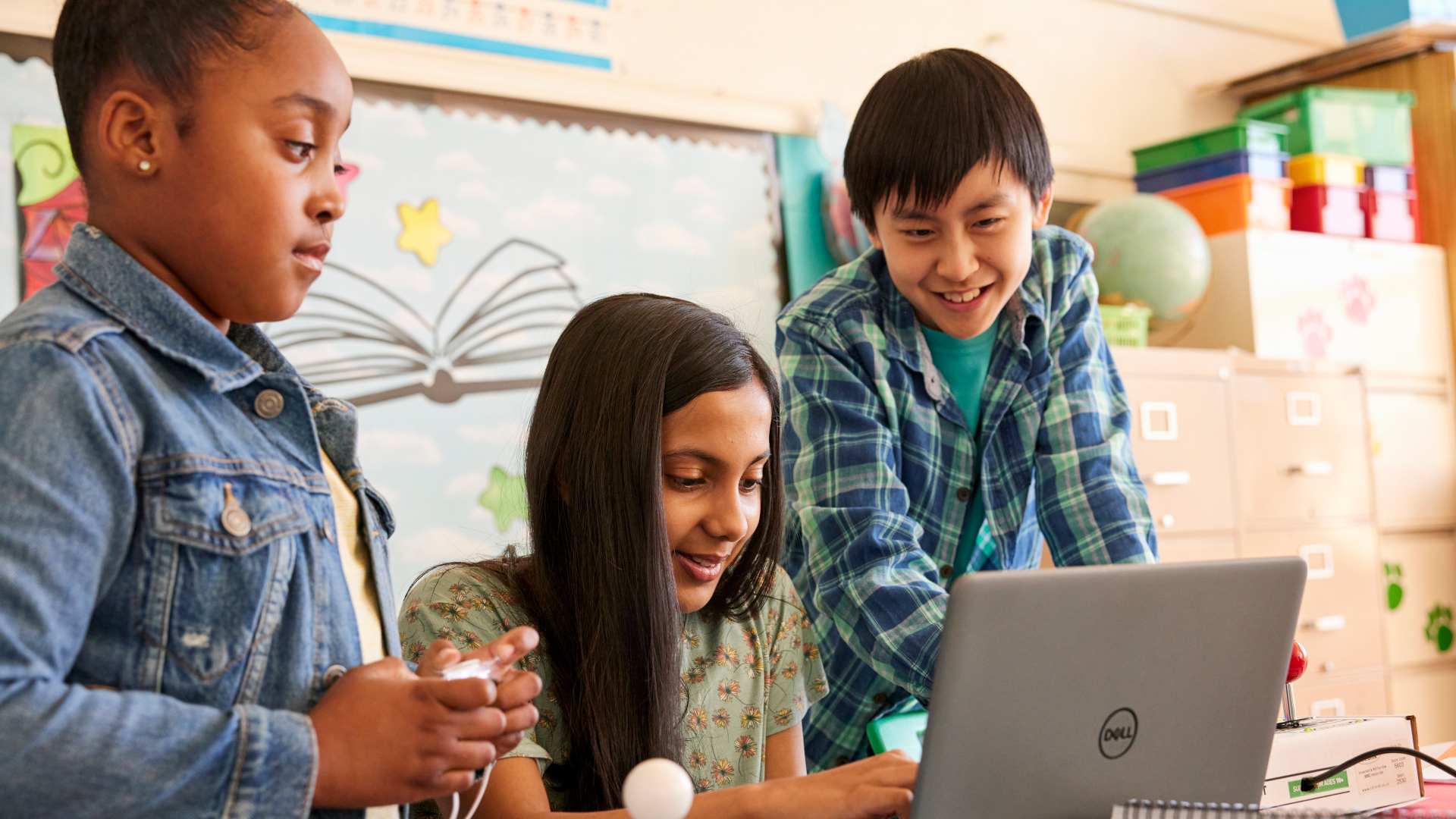 Three students working together on a laptop in a school classroom.