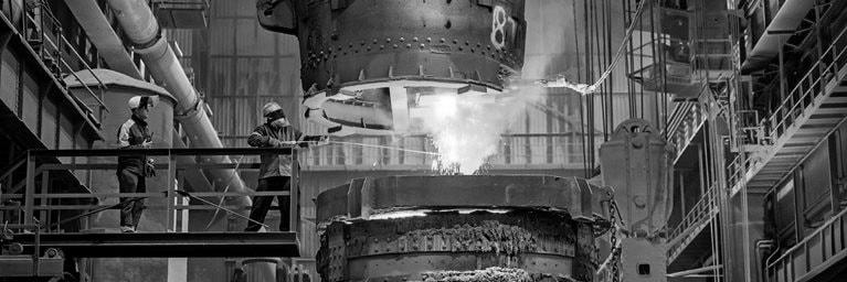 Steelworkers in heat protective gear starting a glowing molten steel pour in a steelworks factory.