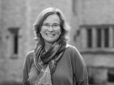 Portrait photograph of Professor Helena Hamerow, a white lady with shoulder length light brown hair and glasses. She stands outside University of Oxford College buildings.