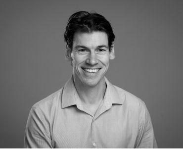 Portrait of Professor Francis Brown, a white man with short dark hair wearing a light blue shirt. He is in front of a neutral grey background.