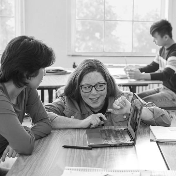 An educator in a school classroom engages with a student at the student’s desk.