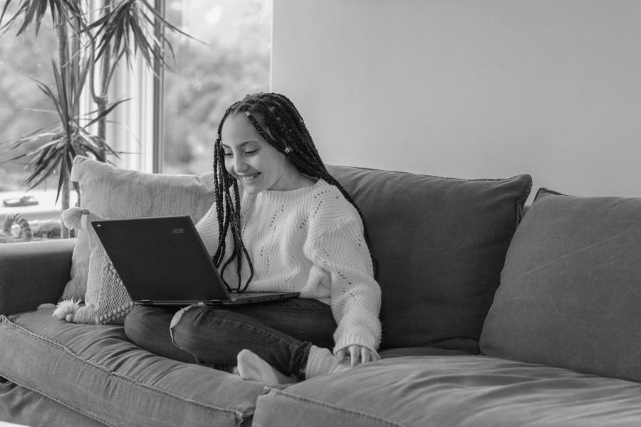 A student looking at a laptop screen while sitting on a couch at home.