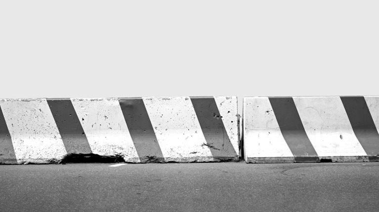 A pair of red and white concrete road barriers aligned on a street against a light blue background.