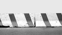 A pair of red and white concrete road barriers aligned on a street against a light blue background.