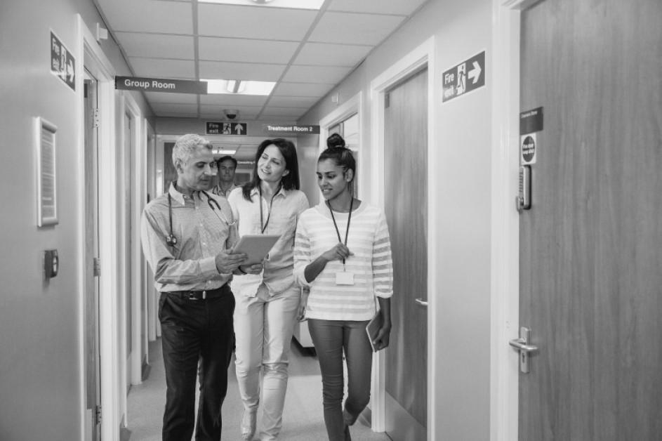 Three doctors meet in the corridor and chat along the way looking at a digital tablet.